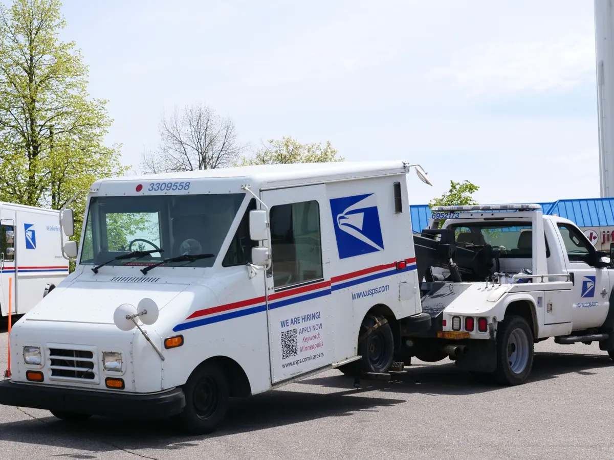 A United States Postal Service (USPS) mail truck is being towed outdoors on a clear day.