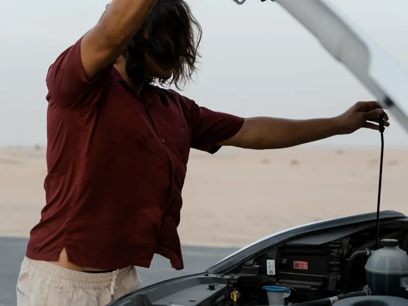 A man examines the engine of a car on a deserted road, highlighting automotive maintenance.