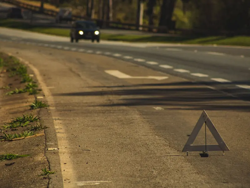 Automobile with headlights on driving on asphalt road with triangular sign in twilight