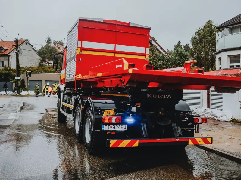 A red tow truck parked on a wet street in an urban neighborhood with workers in the background.
