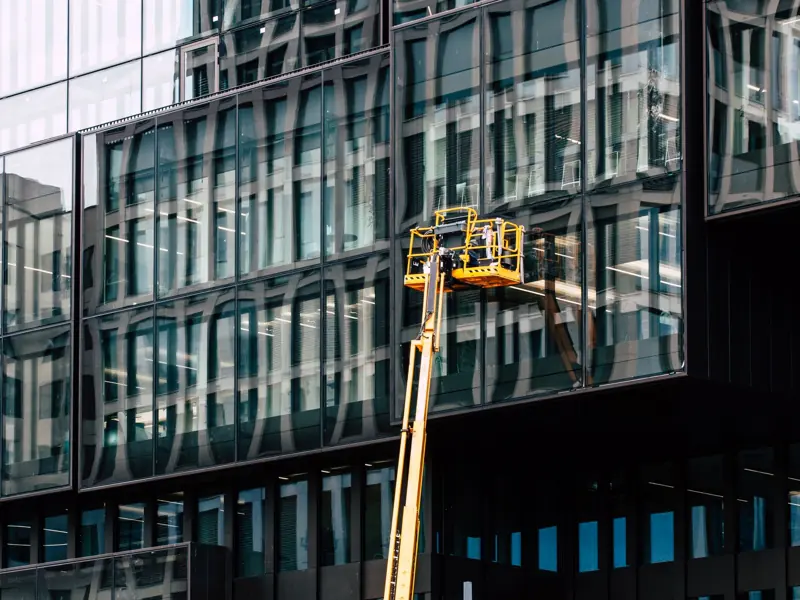Workers on a lift cleaning windows of a modern glass building exterior.