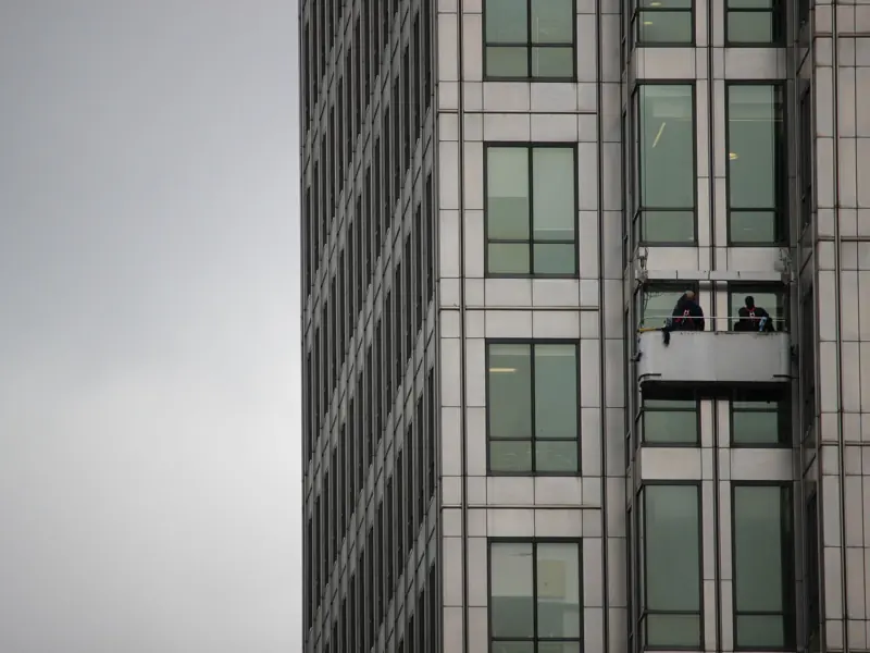 Window cleaners working on a platform on a modern high-rise building on a cloudy day.