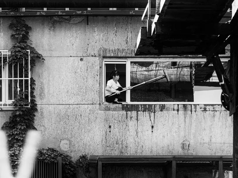 A woman cleaning a window in an urban setting, captured in black and white.