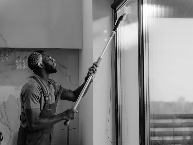 A man cleaning a glass window with a mop in grayscale, showcasing professional work.