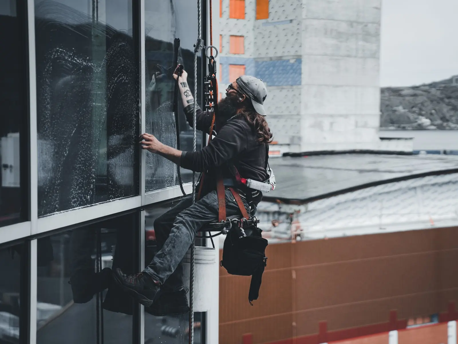 A man cleaning skyscraper windows with a harness, showcasing urban high-rise work.